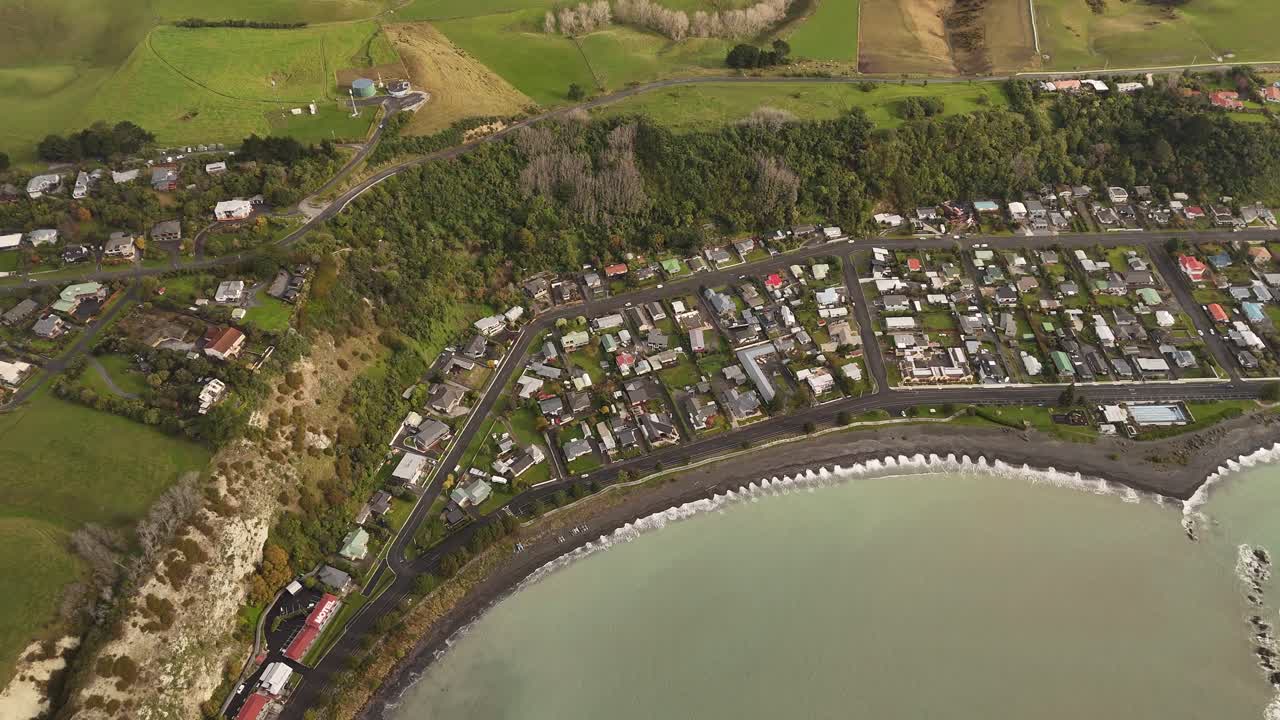 Kaikoura coastal town, houses along dark beach, cliffs, and surrounding green hills, South Island, New Zealand. Aerial top-down view