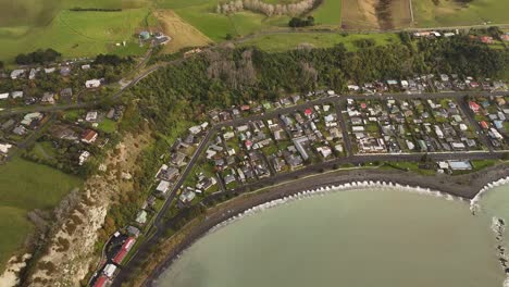 kaikoura coastal town, houses along dark beach, cliffs, and surrounding green hills, south island, new zealand. aerial top-down view
