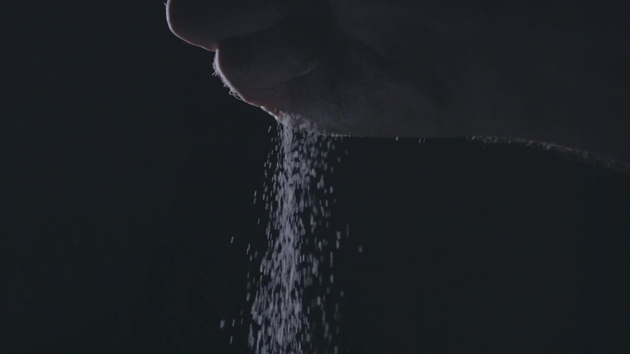 Sugar falling gracefully from a hand in slow motion against a dark background, close-up