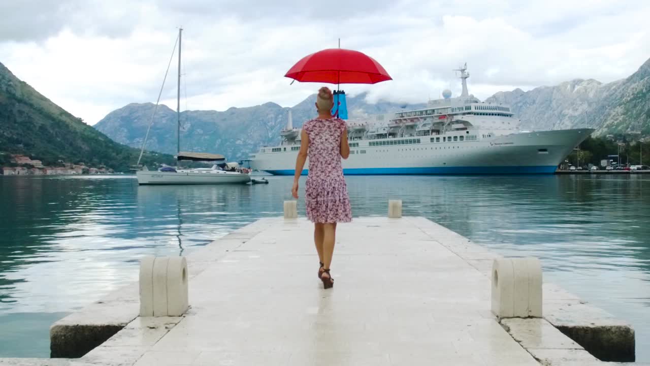 женщина с красным зонтиком, идущая по пирсу