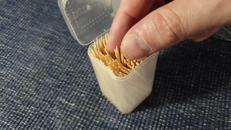 abriendo cuidadosamente la caja de plástico de un palillo puntiagudo y afilado y seleccionando solo un palillo con los dedos
