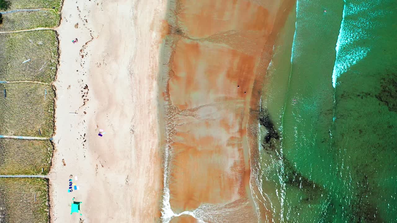 Bird’s-eye aerial drone flying over busy Saco, Maine beaches. People crowd the sandy shore near vacation houses while the Atlantic Ocean’s waves crash along the lively summer coastline on East Coast