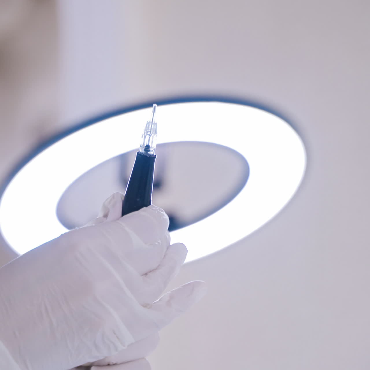 A permanent makeup master checks his professional instrument before performing the procedure in the room on the background of lamp. Close-up. Blurred background.