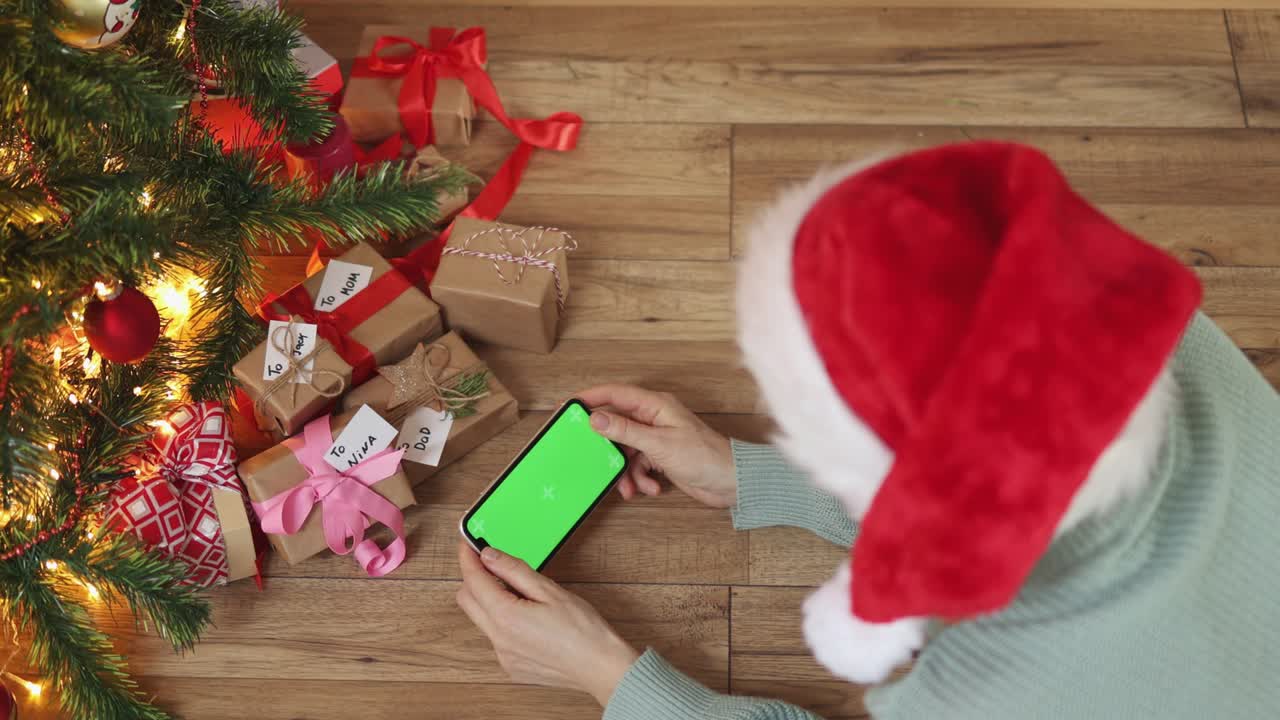 sombrero de navidad rojo femenino manos de teléfono inteligente pantalla verde bajo cajas de regalos de abeto