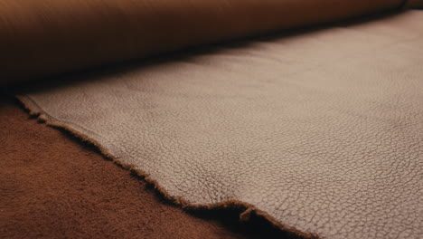 closeup shot of a wrapped up leather hide being rolled open on a table in a workshop, revealing the rustic texture on the surface of the leather. 4k
