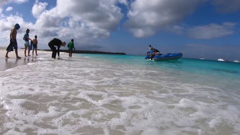 a boat is approaching the shore of a white sand and turquoise water beach of the galapagos islands while tourists are coming close to the boat to board it