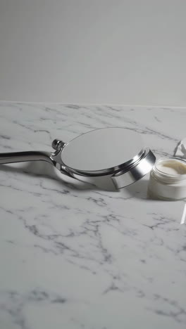open jar of facial cream on marble surface with cotton pads