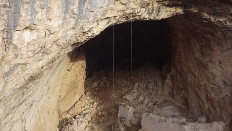 rock climbers climbing on ropes above a massive cave