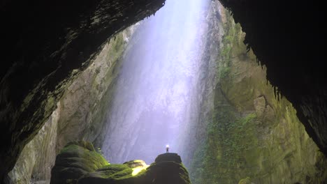 rayo de sol brillando sobre una persona diminuta de pie sobre una estalagmita dentro de una cueva gigantesca