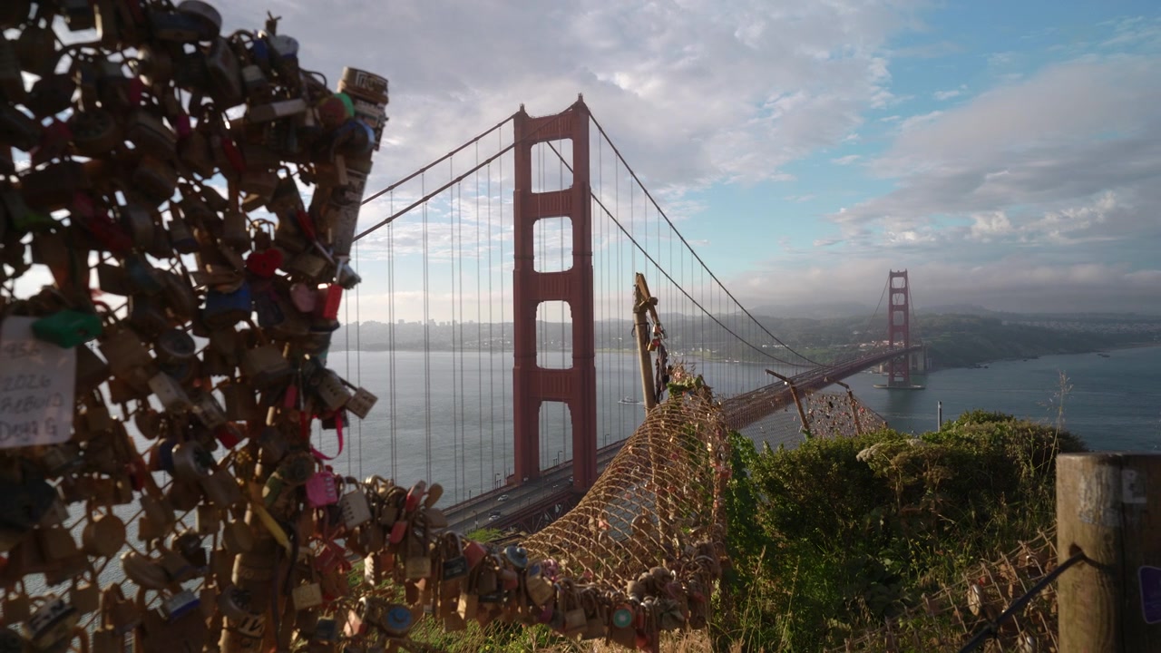 Håndholdt opptak av Golden Gate Bridge bak et gjerde dekket av hengelåser