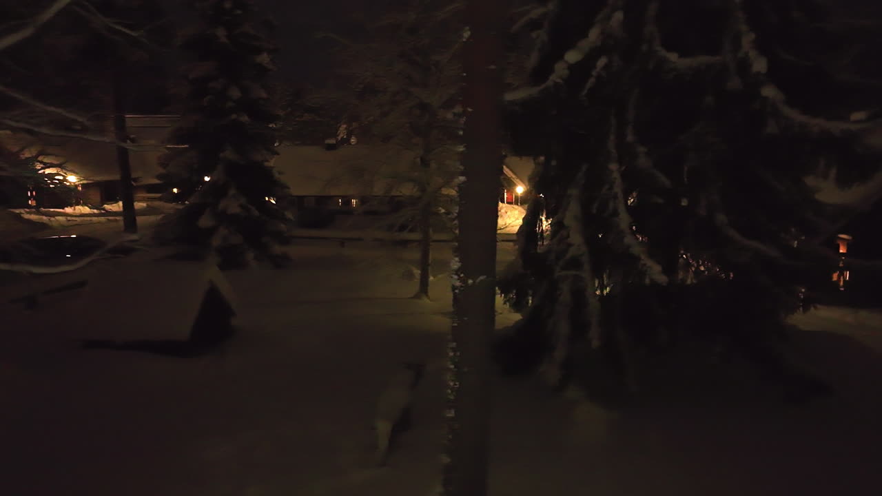 Aerial tracking shot low in middle of snowy trees and cabins, night in Finland