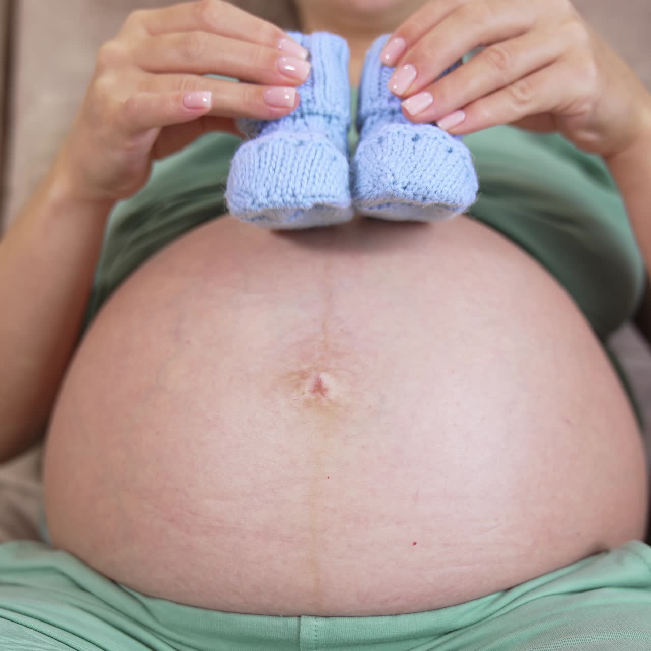 Pancia di una ragazza incinta. Futura mamma che gioca con calzini da neonato lavorati a maglia sul suo ventre nudo. Concetto di salute durante la gravidanza. Primo piano