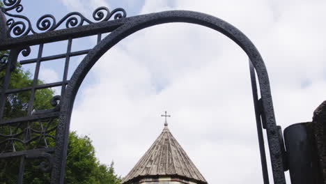 Zooming-through-iron-gate-doorway-arch-on-cross-on-top-of-church-tower