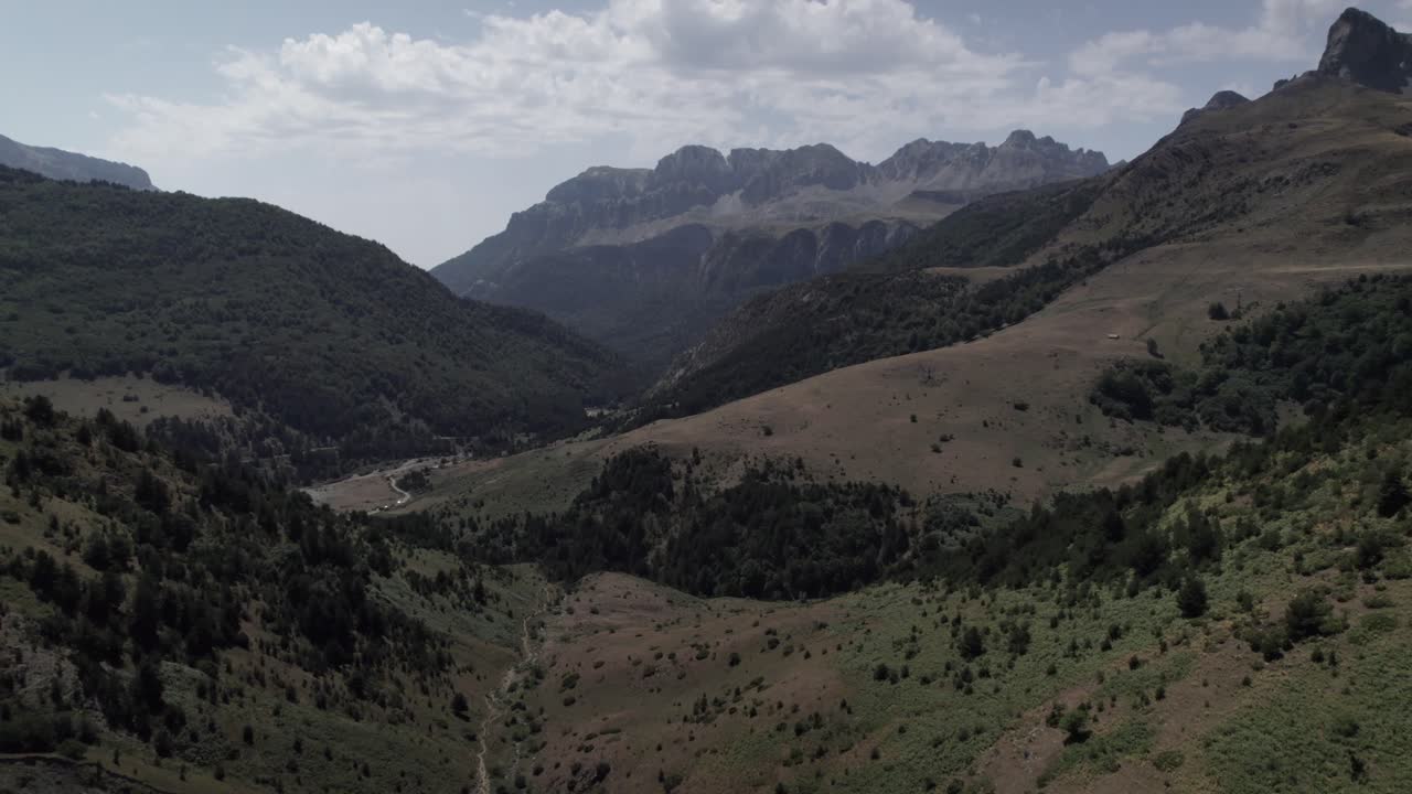 4K ascending drone shot over the Western Valleys Natural Park in the Aragonese Pyrenees, Spain. A cinematic aerial view of the prairie leading to Ibón de Acherito with mountains in the background.