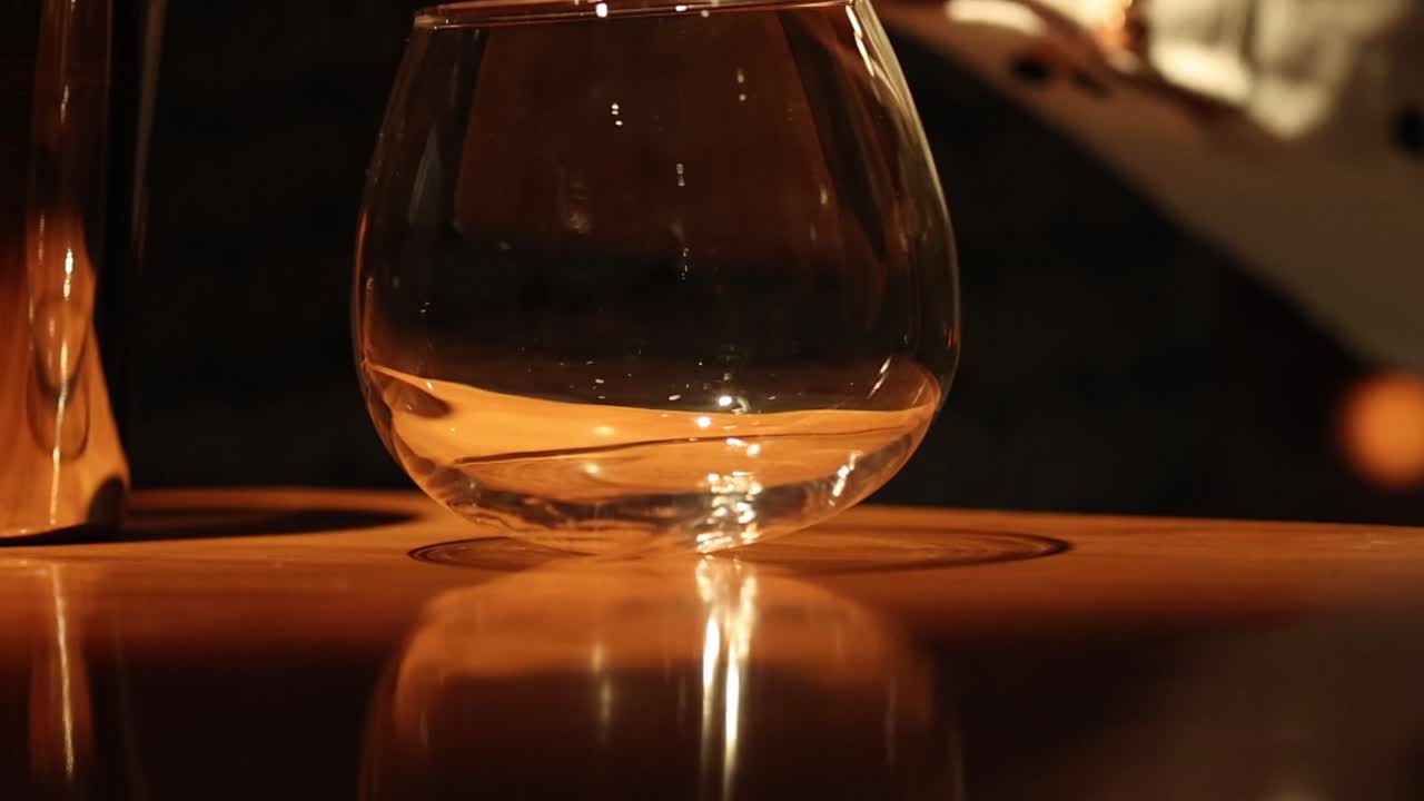 A sequence showing an empty glass reflecting light on a wooden bar surface.
