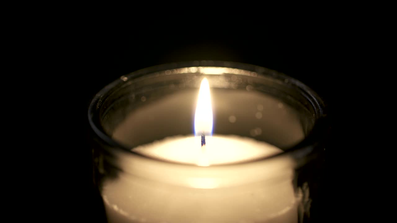 Filmato macro in slow motion di una candela bianca su sfondo scuro