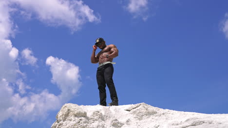 athlete man showing muscles on rocky mountain. handsome black african american man bodybuilder with naked torso posing on the rocky mountain peak