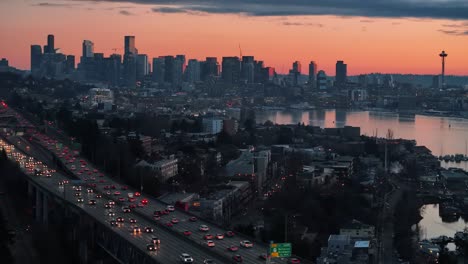 traffic smoothly flows on a highway near dense buildings and lake union with the skyscraper seattle skyline and space needle in the background during a hazy sunset