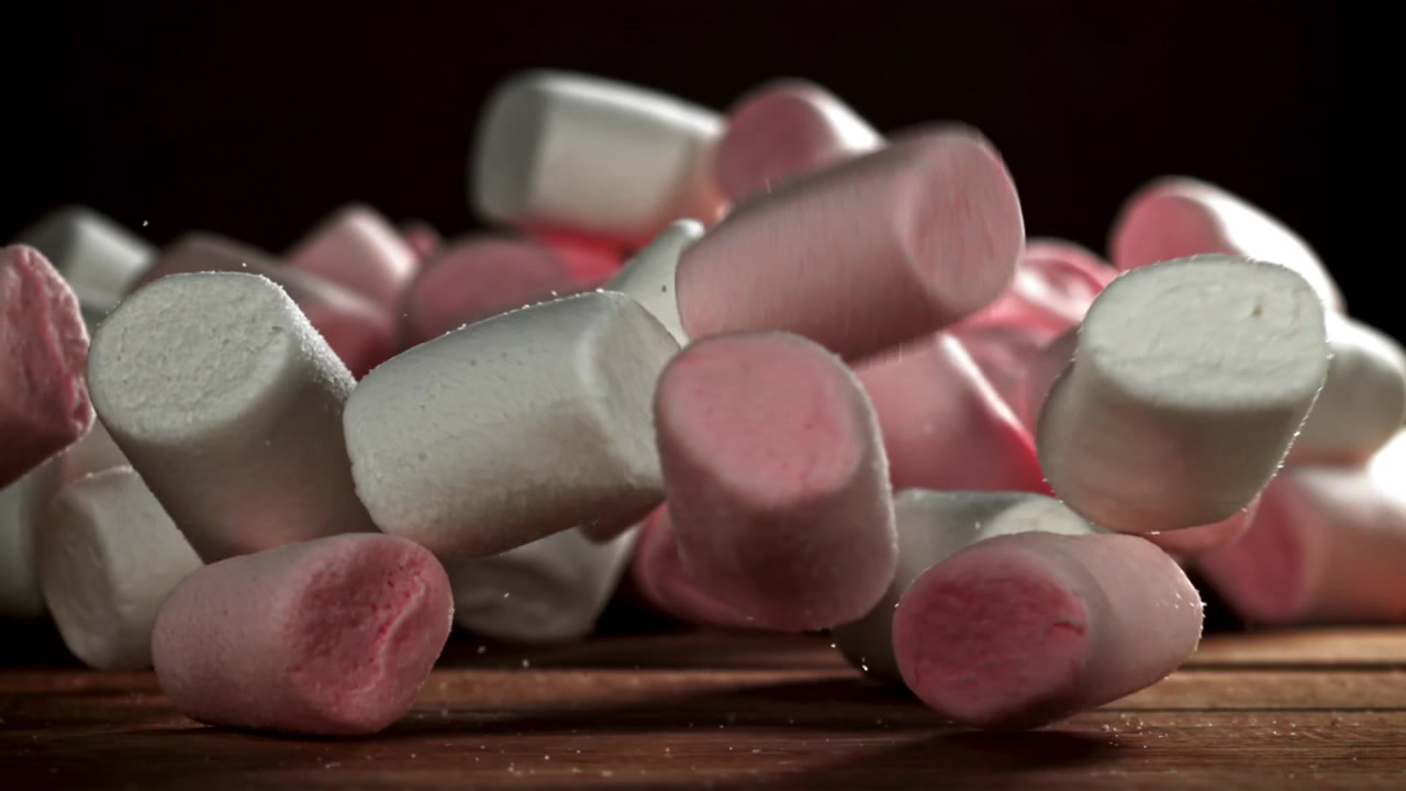 Marshmallow dolci rosa e bianchi che cadono su un tavolo di legno