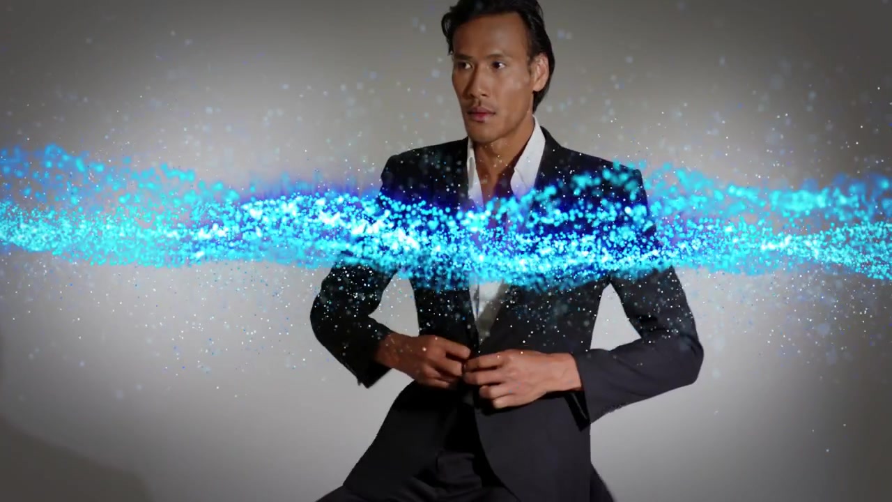 Hombre en un taburete siguiendo una cinta de partículas azules que se extiende, ajustándose la chaqueta del traje y posando para la moda