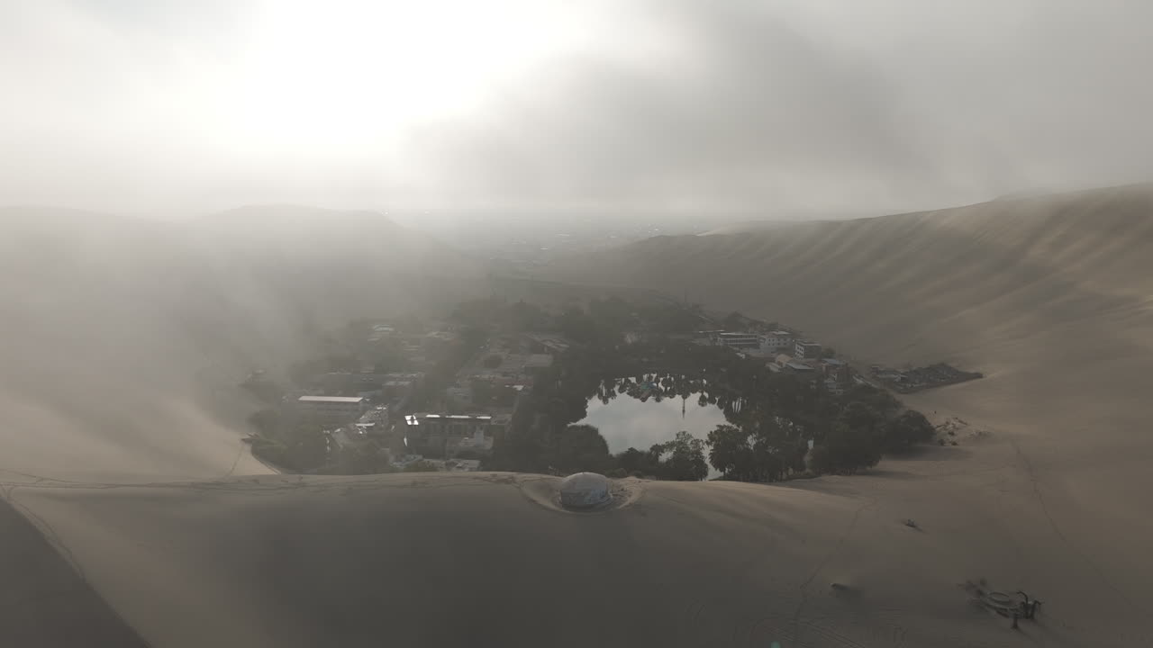 Drone shot revealing the city of Huacachina in Peru behind the dunes on a cloudy day during the mist LOG
