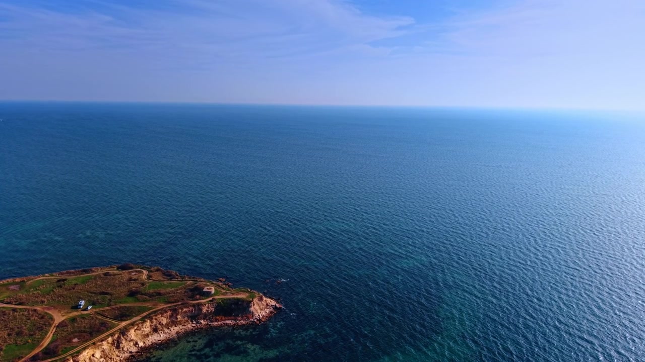 Promontorio costiero roccioso con campi verdi che si protendono in un mare blu calmo. Sentieri sterrati attraversano un promontorio roccioso piatto e verde che termina in scogliere spettacolari che si tuffano in acque costiere limpide e blu.