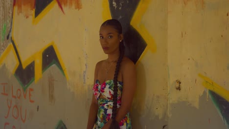 a young woman with sexy eyes stands at a wall with gafitti art in an abandoned building