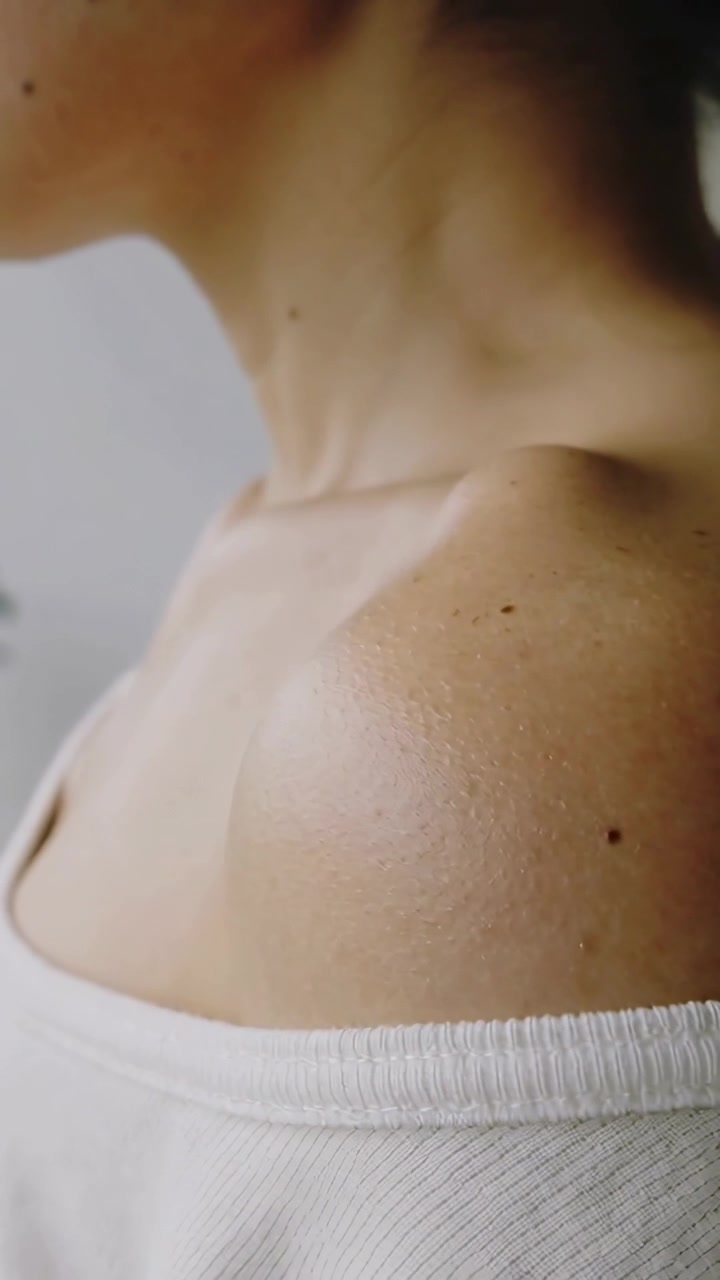 Video verticale: Donna asiatica che si gira, posa e fa scivolare un top bianco a spalle scoperte in una stanza con luce soffusa