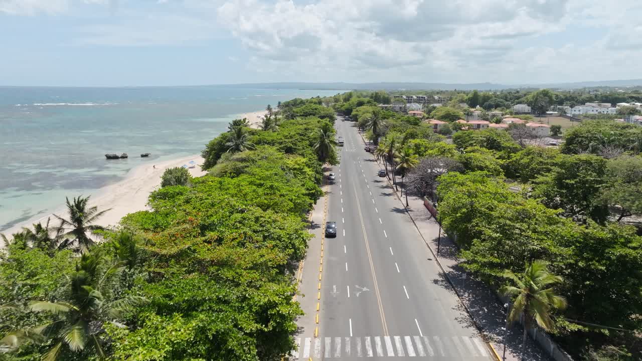 Traffic on coastal road in puerto plata at sunny day. Palm trees and beach with Caribbean Sea on Dominican Republic island. Aerial Birds Eye shot