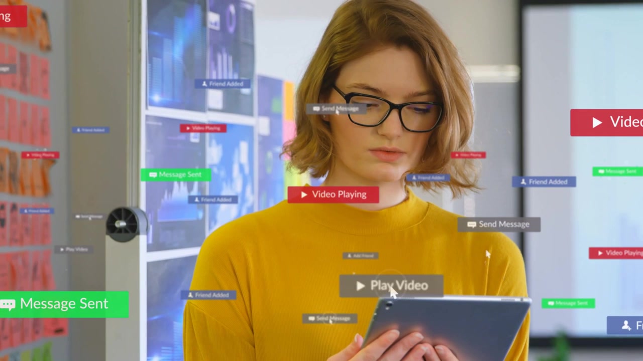 Woman holding tablet in tech office, looking down and causing UI badges to appear, managing media