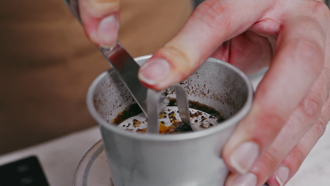 A barista's hand pressing a stainless steel Vietnamese coffee filter , forcing coffee grounds with water and preparing coffee