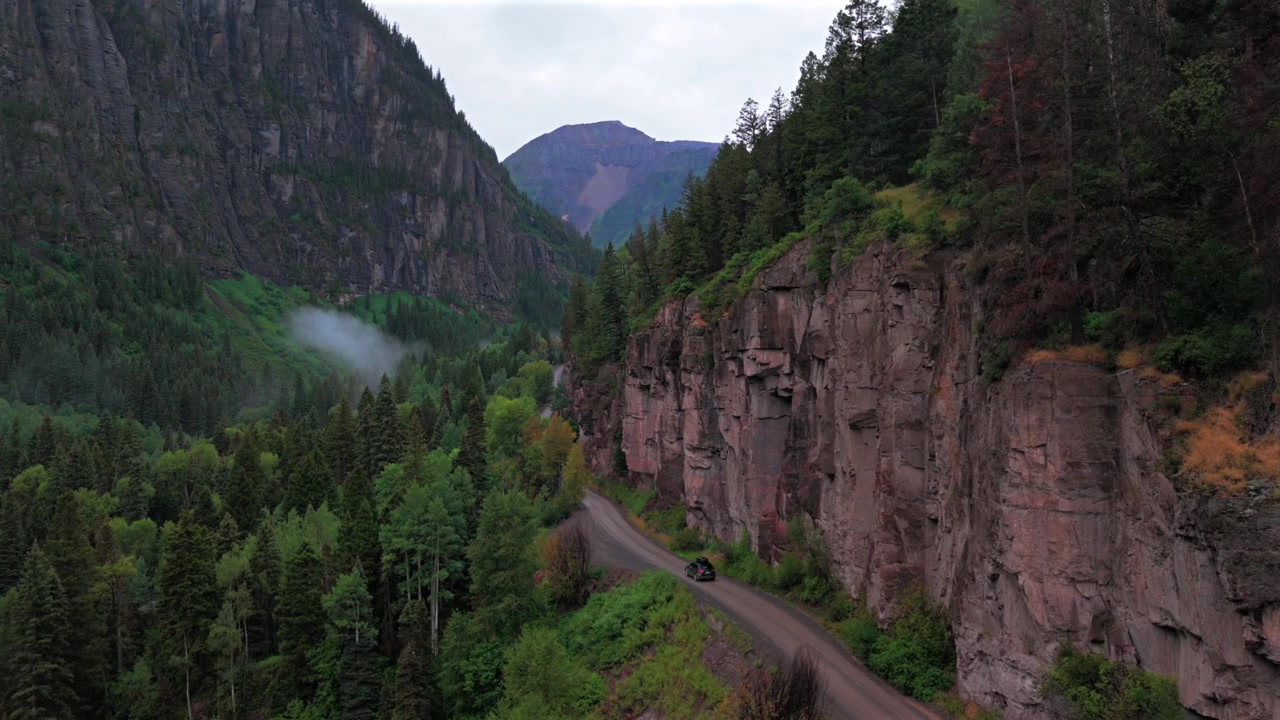 Coche conduciendo en Ouray, Colorado, vista aérea de dron de Yankee Boy Basin, carretera de tierra 4x4 AWD, tarde de verano lluviosa y nublada, Telluride, arroyo Mount Sneffels, Cordillera de San Juan, Montañas Rocosas, paneo hacia adelante.