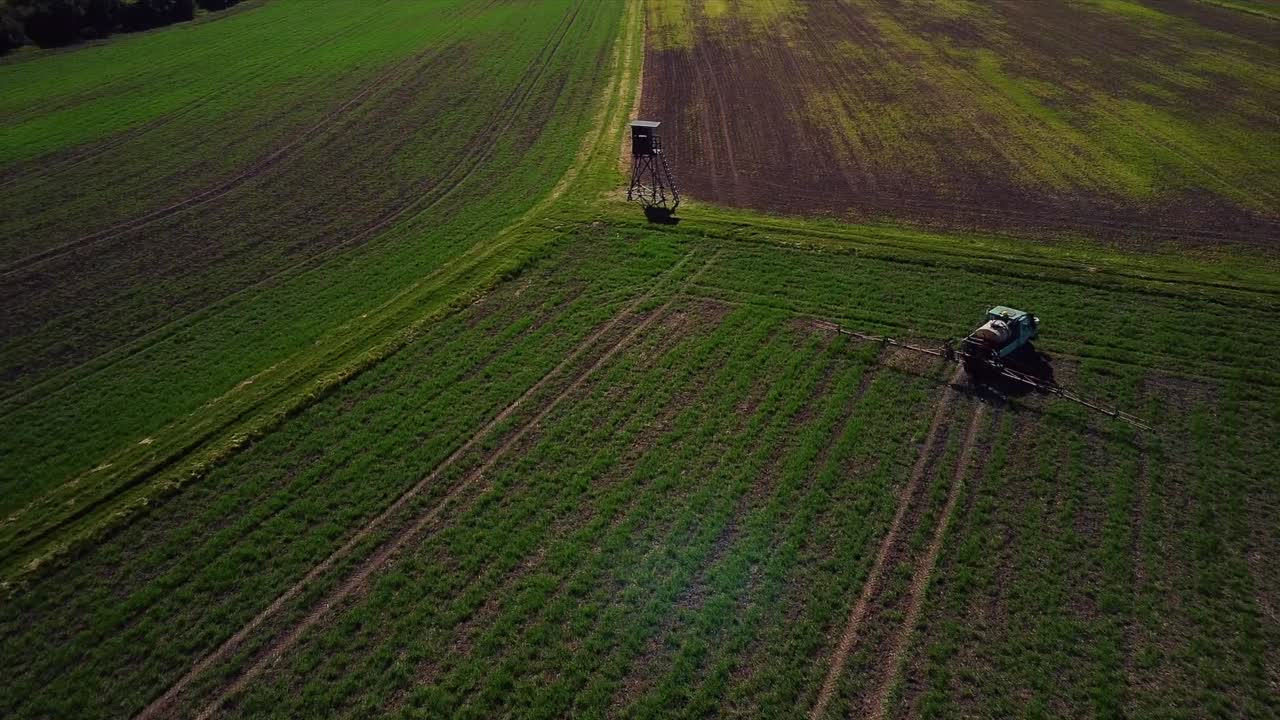 Riprese aeree di un drone che osserva un trattore irrigare i campi verdi e girarsi nella fila successiva mentre il sole tramonta sull'Europa.