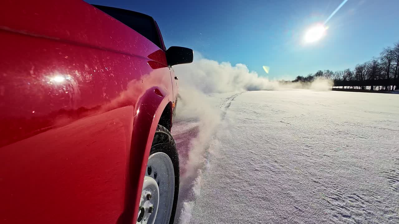 Rød pickup-truck driver i dyb sne med hvid røg og solstråler.