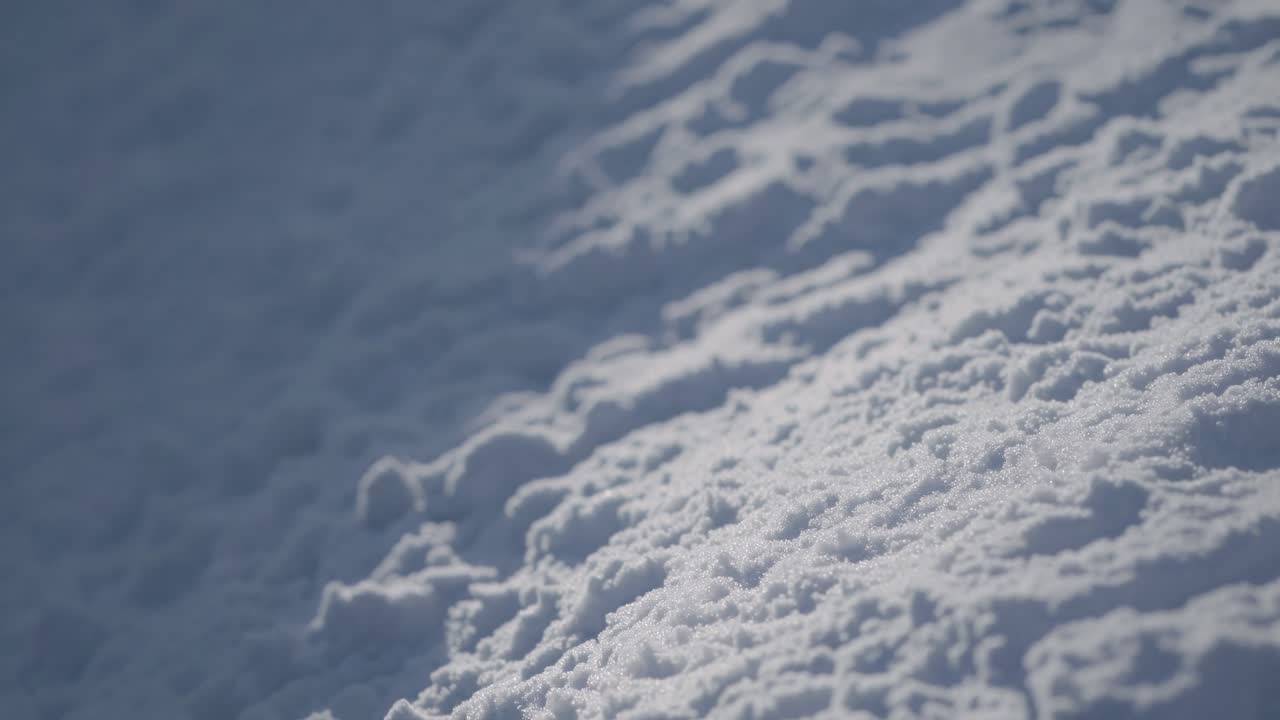 Close-up video of textured snow surface, captured at a low angle, highlighting intricate patterns