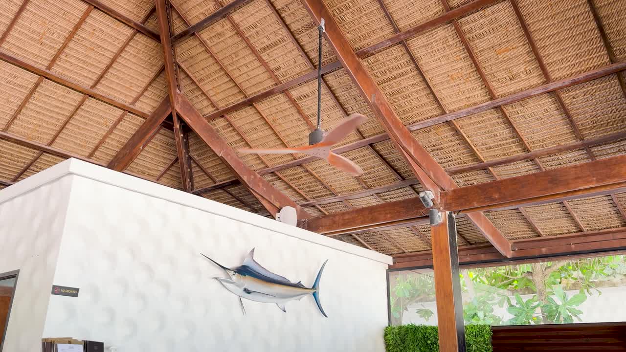 A rustic hut in Phuket with a wooden ceiling fan and marlin decor under a straw roof, captured in natural light