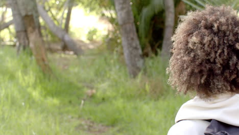 una joven de dos razas con el cabello rizado mira hacia un exuberante entorno al aire libre verde con espacio de copia