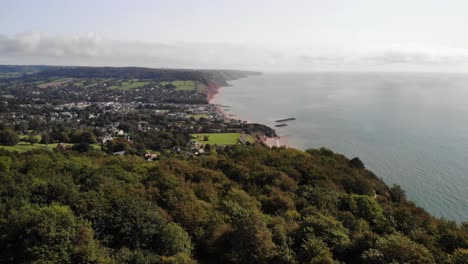 Luftaufnahmen-Fliegen-über-Bäume-Mit-Blick-Auf-Sidmouth-Und-Lyme-Bay,-Devon,-Großbritannien