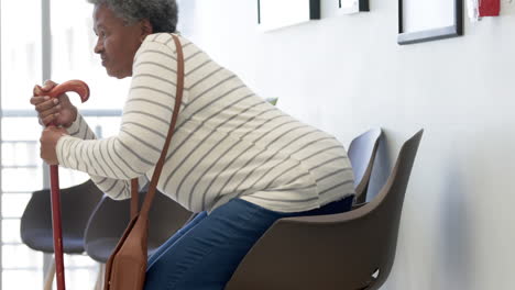 African-american-senior-woman-with-cane-sitting-in-hospital-waiting-room,-slow-motion