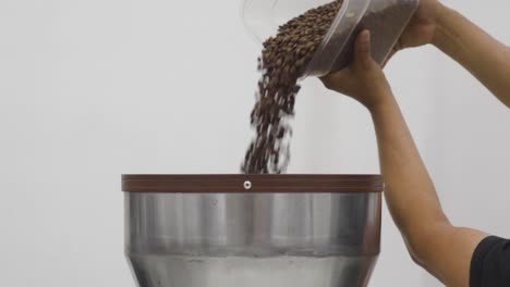 man fills the funnel of coffee grinder with coffee beans