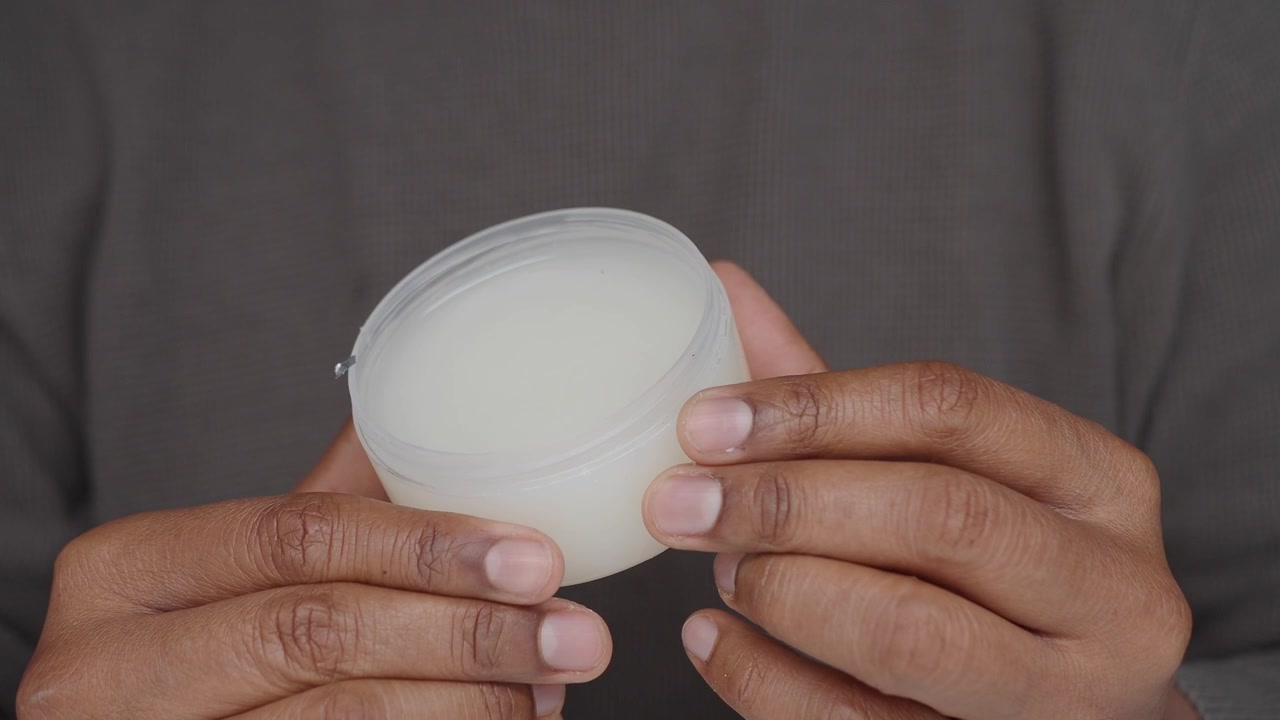 Primer plano de manos sosteniendo un pequeño frasco de crema blanca