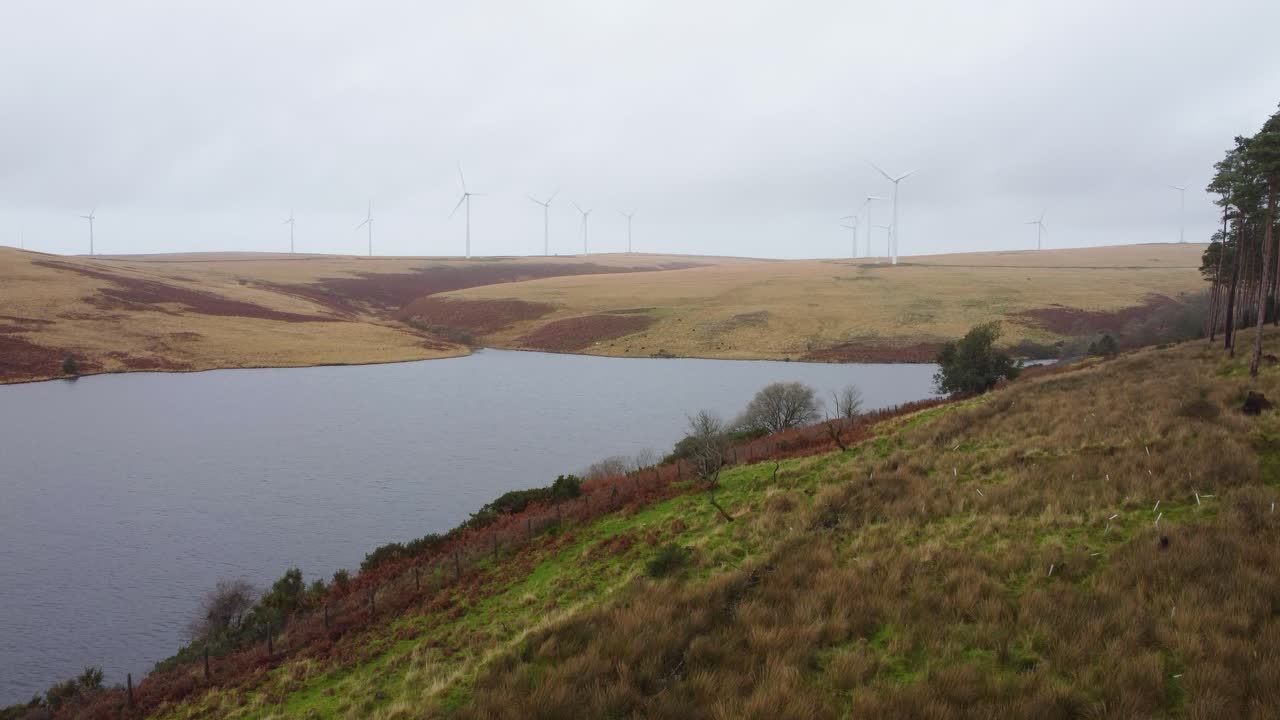 drone aéreo en ascenso sobre el embalse de lliw con turbinas eólicas en el fondo con camino y valla 4k