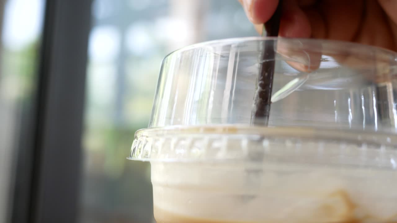 젊은 여성의 손의 클로즈업은 휴가 동안 카페에서 휴식을 취하기 위해 플라스틱 커피 컵에 얼음을 어줍니다.