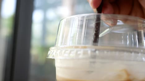 primer plano de la mano de una mujer joven agita el hielo en una taza de café de plástico con paja para relajarse en el café durante las vacaciones.