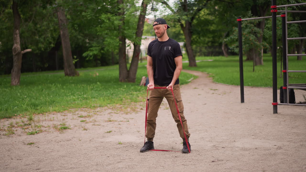 Man Checks Band, Individual Preparing Exercise Band Outdoors, Man Adjusts Resistance Band In Park Before Workout, Person Ensuring Resistance Band Is Secure Prior To Outdoor Fitness Routine