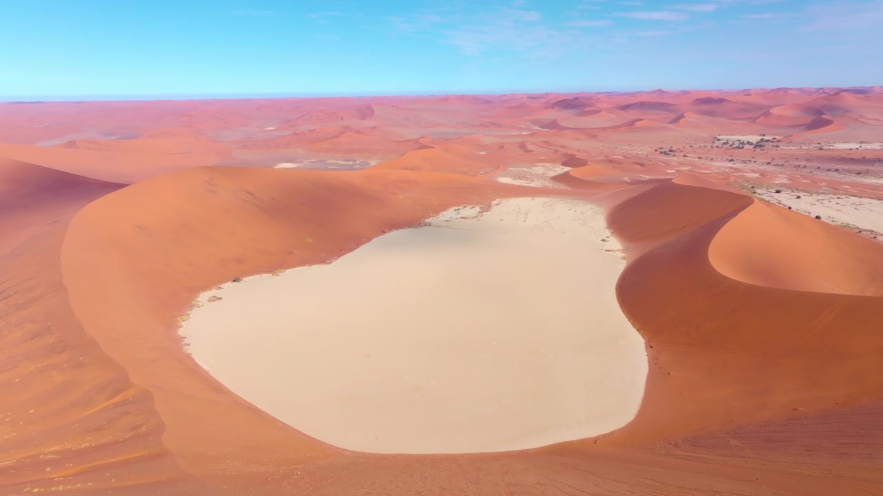Vista de drone sobre as imponentes dunas de areia vermelha e a planície de argila branca de Sossusvlei no Parque Nacional Namib-Naukluft. Imponentes dunas vermelhas brilham sobre planícies de argila pálidas.