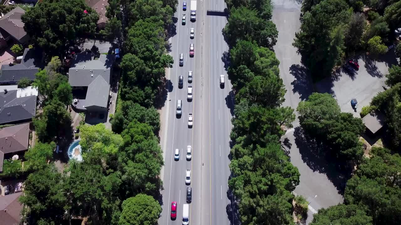 tráfico de carretera cuatro carriles que van en direcciones opuestas rodeados de árboles y casas suburbanas