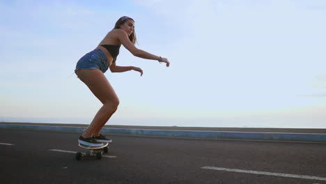 enjoying the serene sunset, a woman skateboarder rides along a road in slow motion, with mountains and a stunning sky as the backdrop. she wears shorts