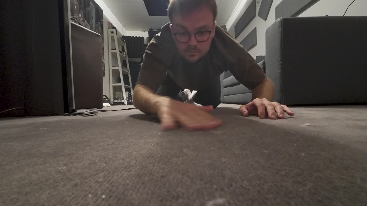 A man is on his hands and knees, looking closely at the floor as if searching for a lost item