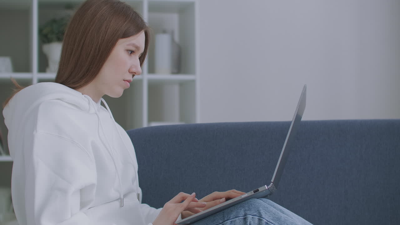 집에서 소파에 노트북을 사용하는 여성. 소파에 컴퓨터와 함께 앉아서 밖을 바라보는 사려 깊은 젊은 여성은 집에서 원격으로 일하는 데 추가적인 동기가 필요합니다.